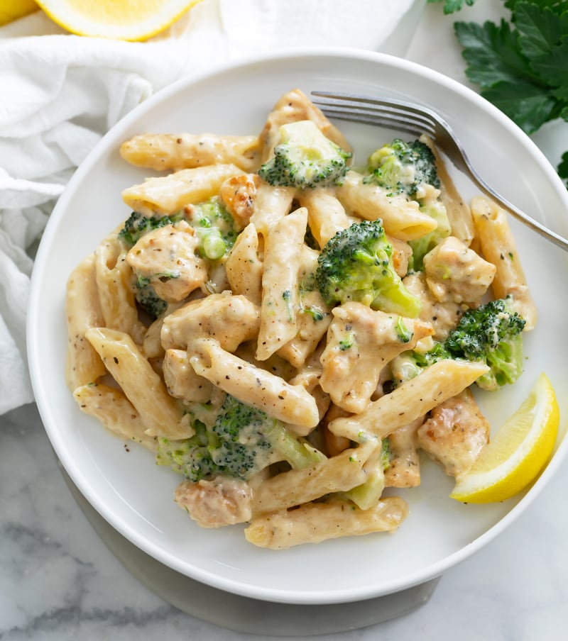 A white plate with Chicken and Broccoli Pasta and a lemon slice.
