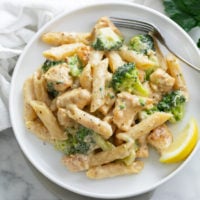 Creamy Chicken and Broccoli Pasta on a white plate with a lemon slice on the side.