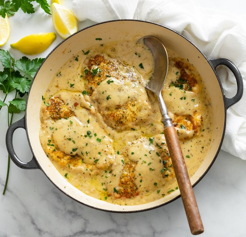 A skillet filled with Chicken in White Wine Sauce with a spoon in it and fresh parsley on top.