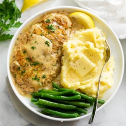 A white plate of Chicken in White Wine Sauce next to mashed potatoes and green beans.