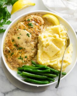 A white plate of Chicken in White Wine Sauce next to mashed potatoes and green beans.