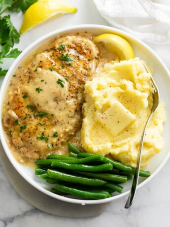 A white plate of Chicken in White Wine Sauce next to mashed potatoes and green beans.