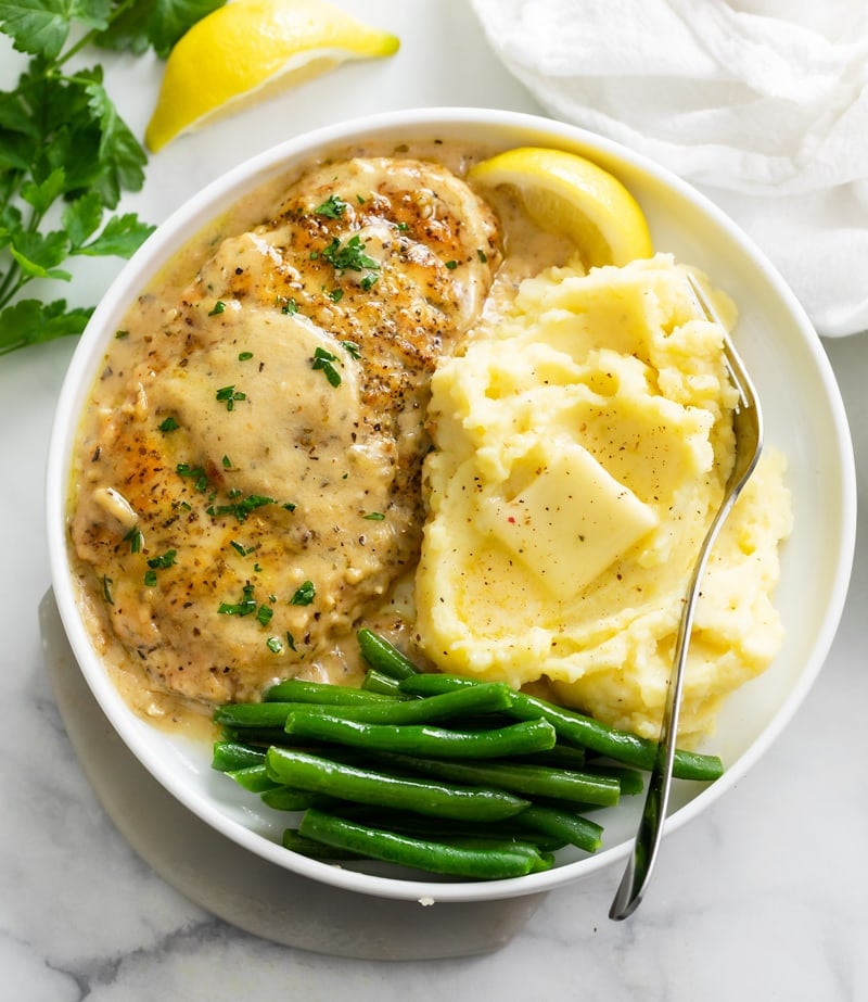 Chicken in White Wine Sauce on a white plate with mashed potatoes and green beans.