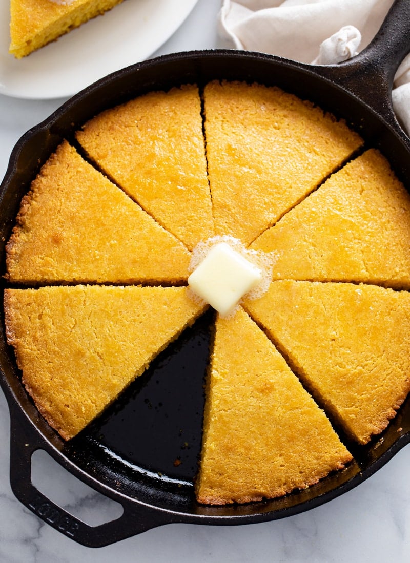 Cornbread in a cast iron skillet with a pat of butter on top.