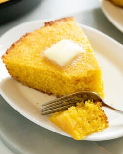 A white plate with a slice of Cornbread with butter on top and a fork.