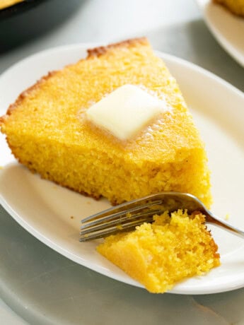 A white plate with a slice of Cornbread with butter on top and a fork.