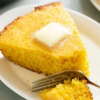 A slice of cornbread on a white plate with butter on top.