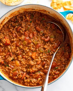 A pot filled with Chili with a ladle in it and Fritos on the side.