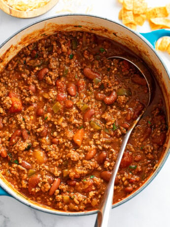 A pot filled with Chili with a ladle in it and Fritos on the side.