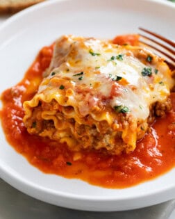 A Lasagna Roll Up on a white plate with sauce and cheese.