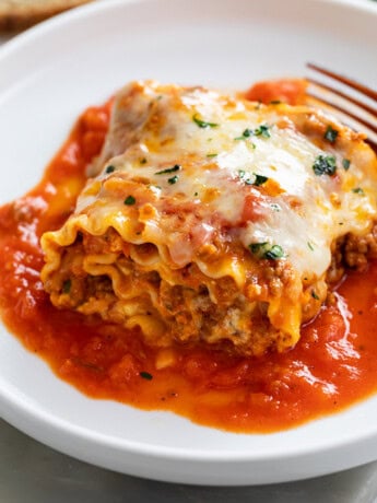 A Lasagna Roll Up on a white plate with sauce and cheese.