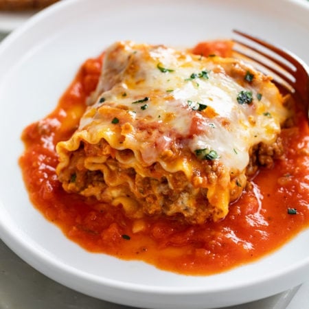 A Lasagna Roll Up on a white plate with sauce and cheese.