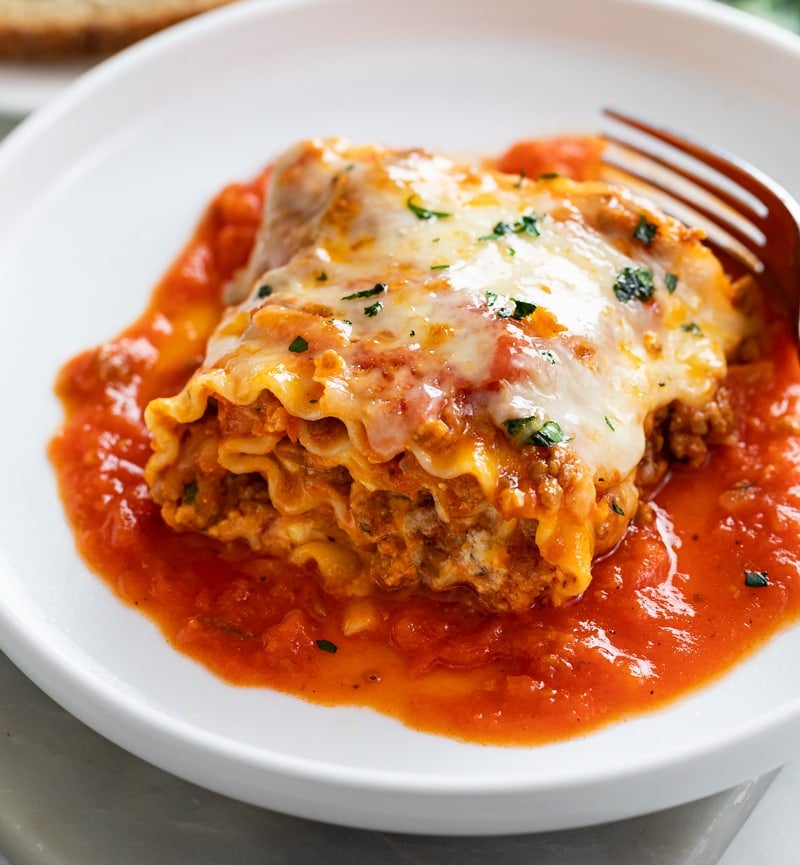A Lasagna Roll Up on a white plate with sauce and cheese.