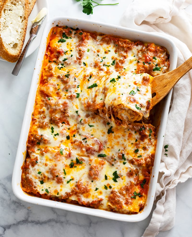 A casserole dish filled with cheesy Lasagna Roll Ups with a spatula pulling one out.