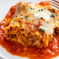 A Lasagna Roll Up on a white plate with marinara sauce and a meat filling with cheese.