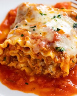 A Lasagna Roll Up on a white plate with marinara sauce and a meat filling with cheese.