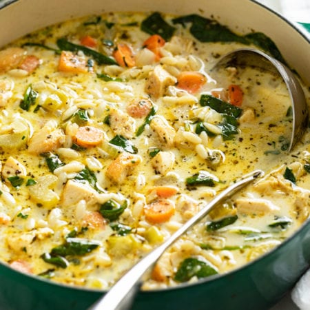 A soup pot with Lemon Chicken Orzo Soup with spinach and vegetables.