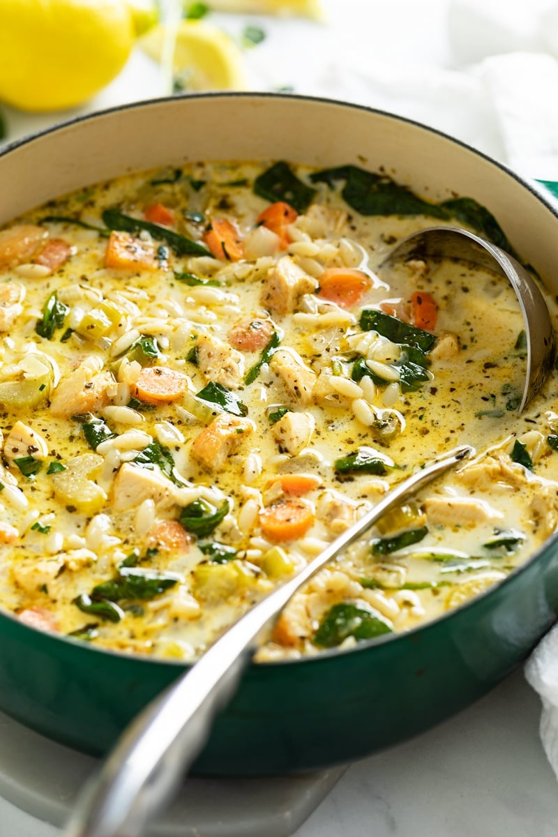 A soup pot with Lemon Chicken Orzo Soup with spinach and vegetables.