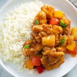 Sweet and Sour Chicken with Peppers and Pineapple on a white plate with rice.