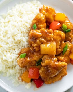 Sweet and Sour Chicken with Peppers and Pineapple on a white plate with rice.