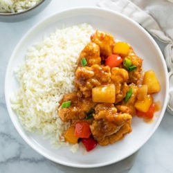 Sweet and Sour Chicken on a white plate next to a bed of white rice.