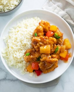 Sweet and Sour Chicken on a white plate next to a bed of white rice.