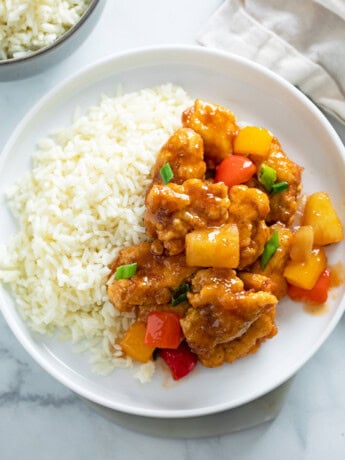 Sweet and Sour Chicken on a white plate next to a bed of white rice.