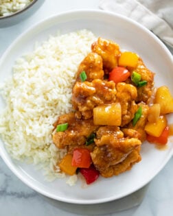 Sweet and Sour Chicken on a white plate next to a bed of white rice.