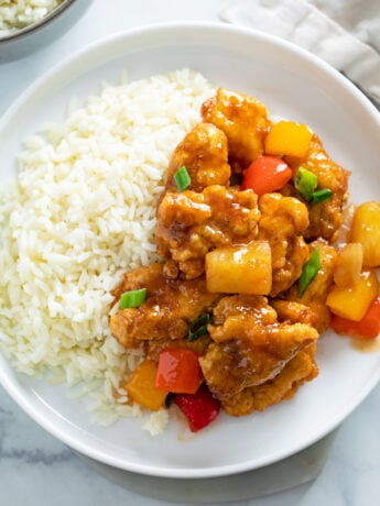 Sweet and Sour Chicken on a white plate next to a bed of white rice.