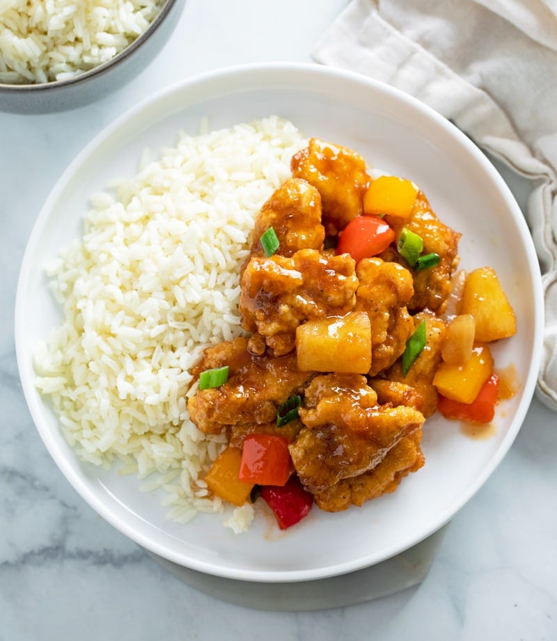 Sweet and Sour Chicken on a white plate next to a bed of white rice.