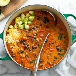 A soup pot filled with Taco Soup with a ladle in it and avocados and cheese on top.
