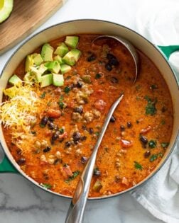 A soup pot filled with Taco Soup with a ladle in it and avocados and cheese on top.