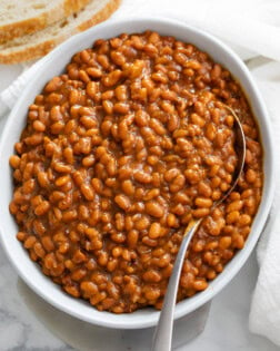 Baked Beans in a white bowl with a spoon and bread on the side.