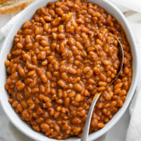A white bowl filled with baked beans with a spoon.