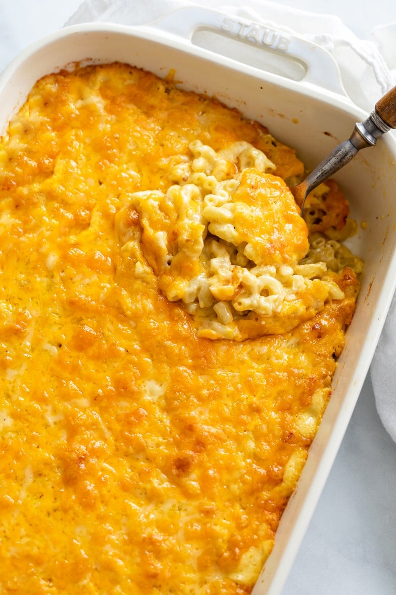 A casserole dish filled with Baked Mac and Cheese with a spoon scooping it up.