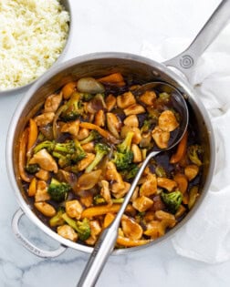 A skillet filled with Chicken and Broccoli with a spoon in it.