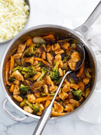 A skillet filled with Chicken and Broccoli with a spoon in it.