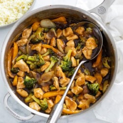 Chicken and Broccoli Stir Fry in a skillet with brown stir fry sauce and a spoon on the side.