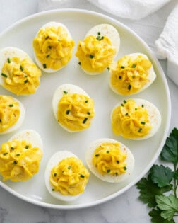 Deviled Eggs on a white plate topped with chives and paprika.