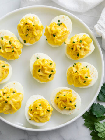 Deviled Eggs on a white plate topped with chives and paprika.