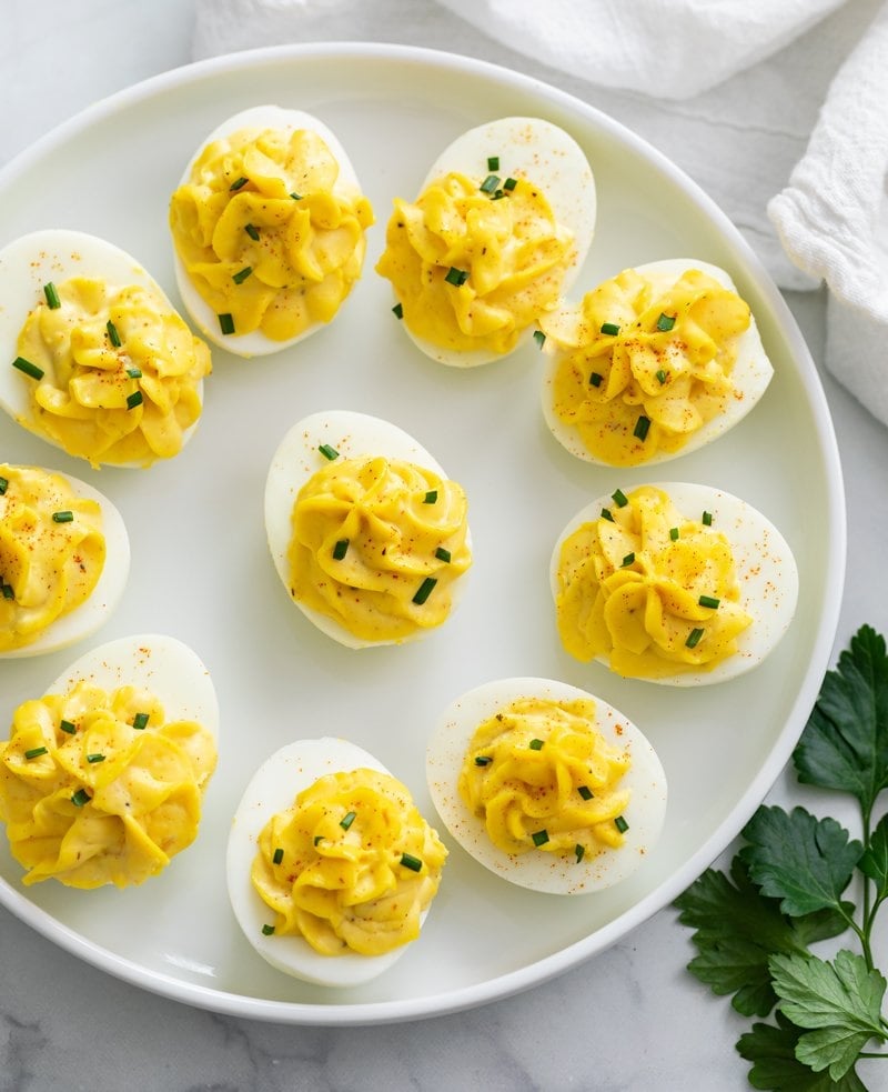 Deviled Eggs on a white plate topped with chives and paprika.