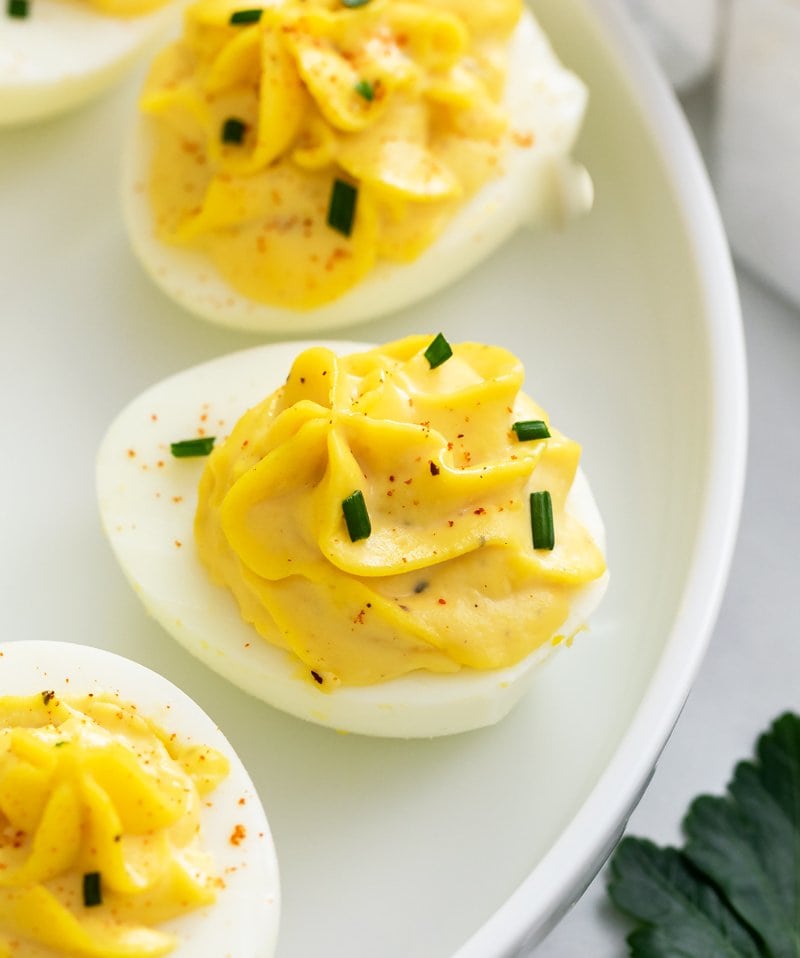 A white plate with deviled eggs topped with paprika and chives.