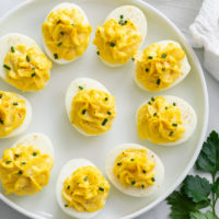 Deviled Eggs on a white plate with paprika and chives on top.