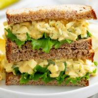 Two halves of an egg salad sandwich stacked on top of each other with lettuce.