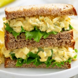 Two halves of an egg salad sandwich stacked on top of each other with lettuce.