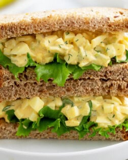 Two halves of an egg salad sandwich stacked on top of each other with lettuce.