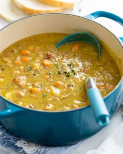 A pot of Split Pea Soup with a ladle in it and fresh thyme on top.