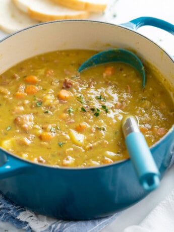 A pot of Split Pea Soup with a ladle in it and fresh thyme on top.