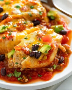 Taco Stuffed Shells on a white plate with cheese, black beans, and avocado.