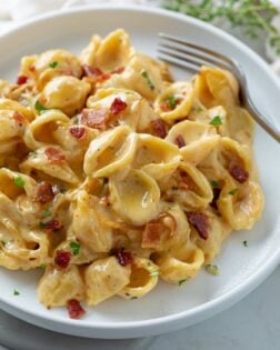 Bacon Mac and Cheese on a white plate with a fork in the back.